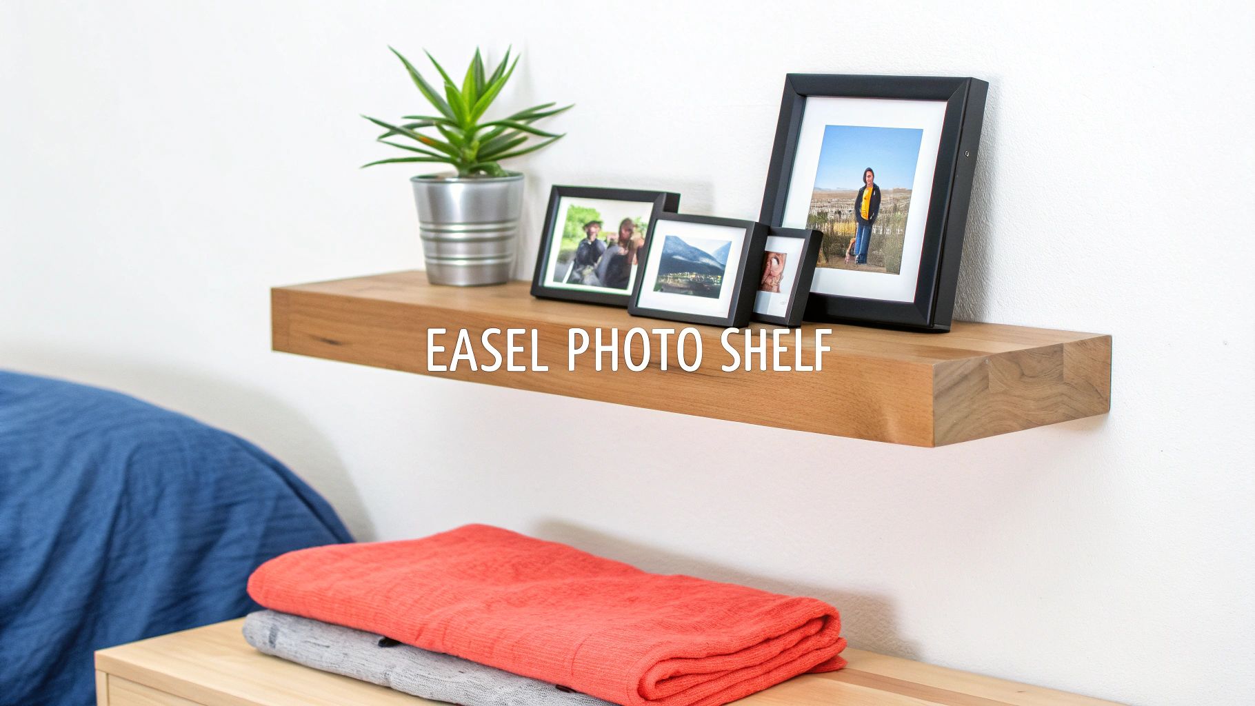 A modern wooden floating shelf holds framed photos and a green potted plant against a white wall.
