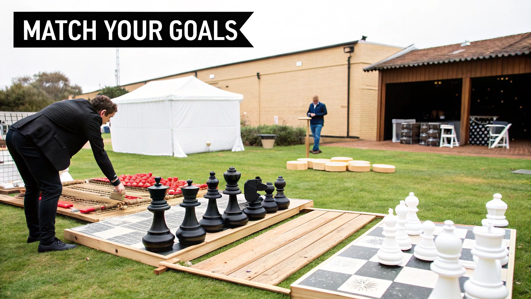 A man arranging pieces on a giant outdoor chess board setup on a green lawn at an event.