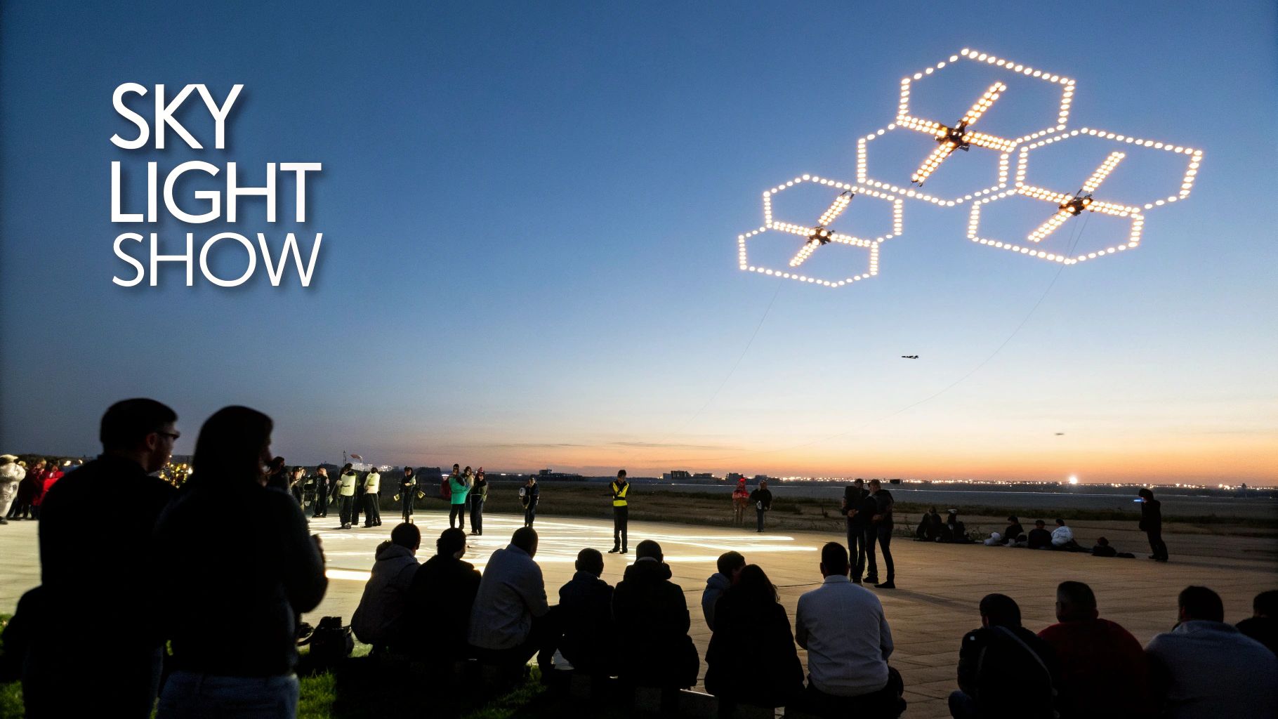People gather at dusk to watch a spectacular drone light show creating glowing hexagonal patterns in the sky.