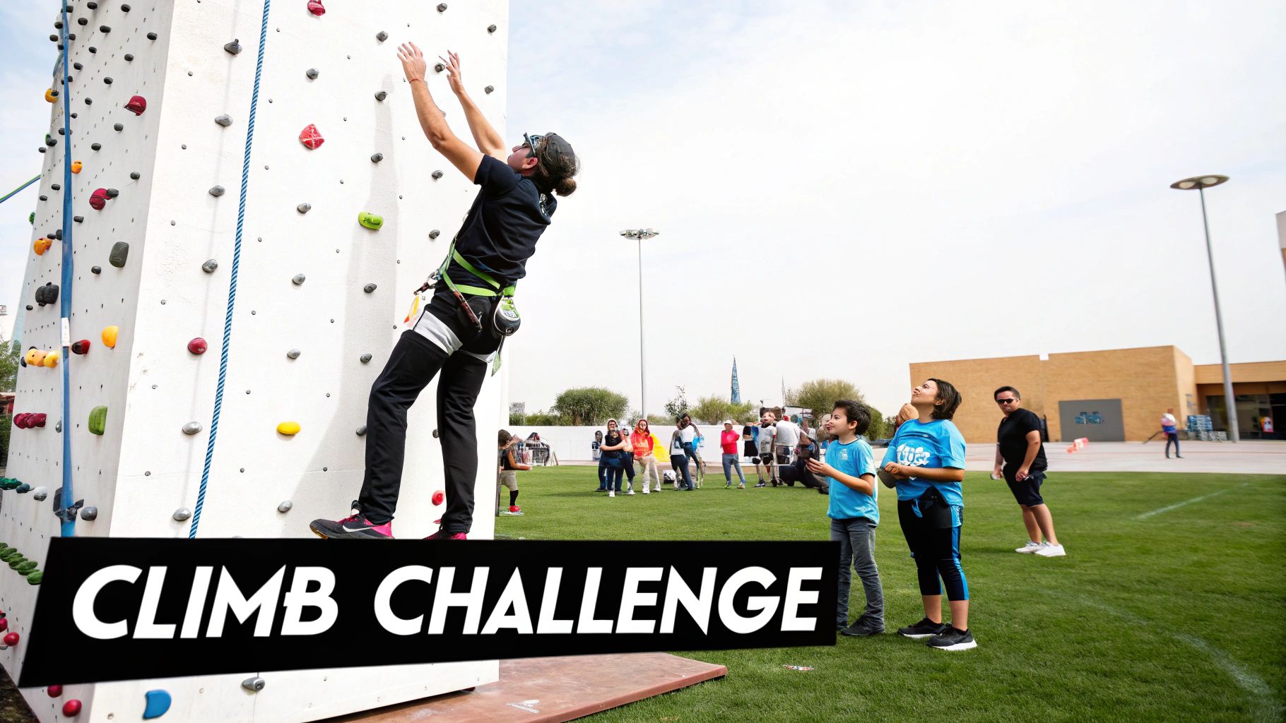 An adult actively rock climbing a challenge wall with colorful holds, watched by children and spectators.