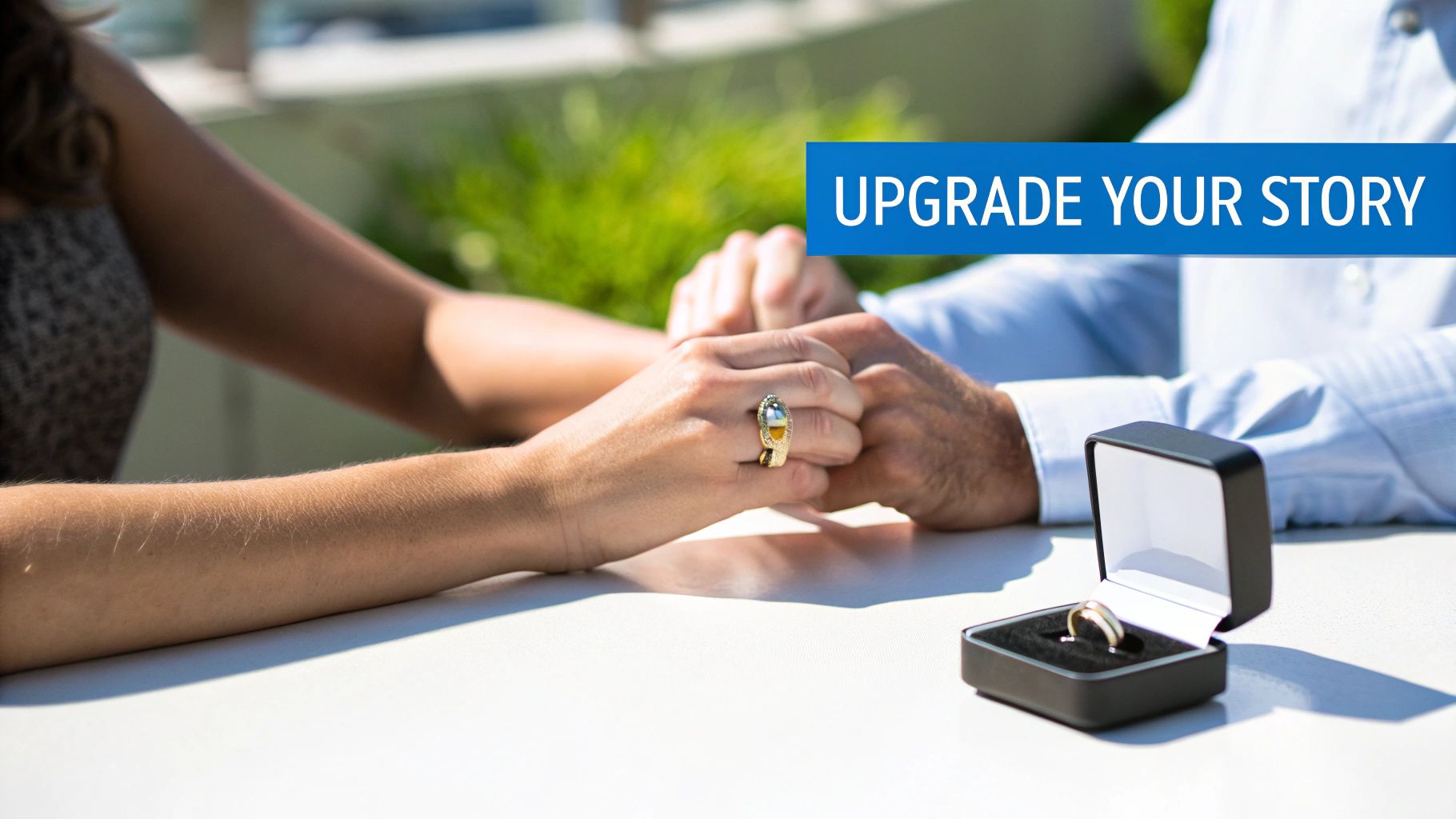 A couple holding hands on a table, one wearing a ring, with another ring in an open box, suggesting an upgrade.