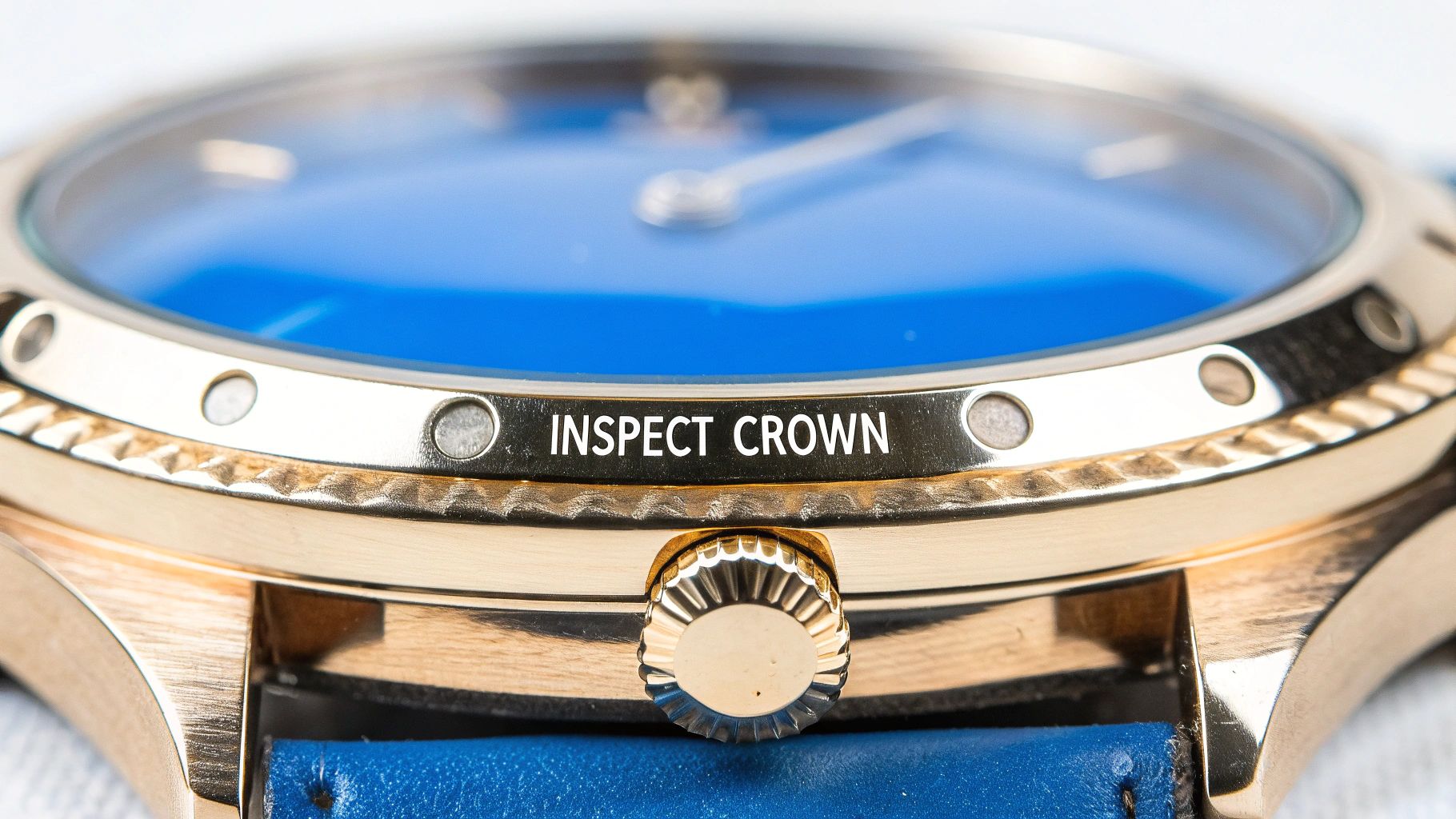 Close-up of a gold watch with a blue face and strap, displaying 'INSPECT CROWN' text.