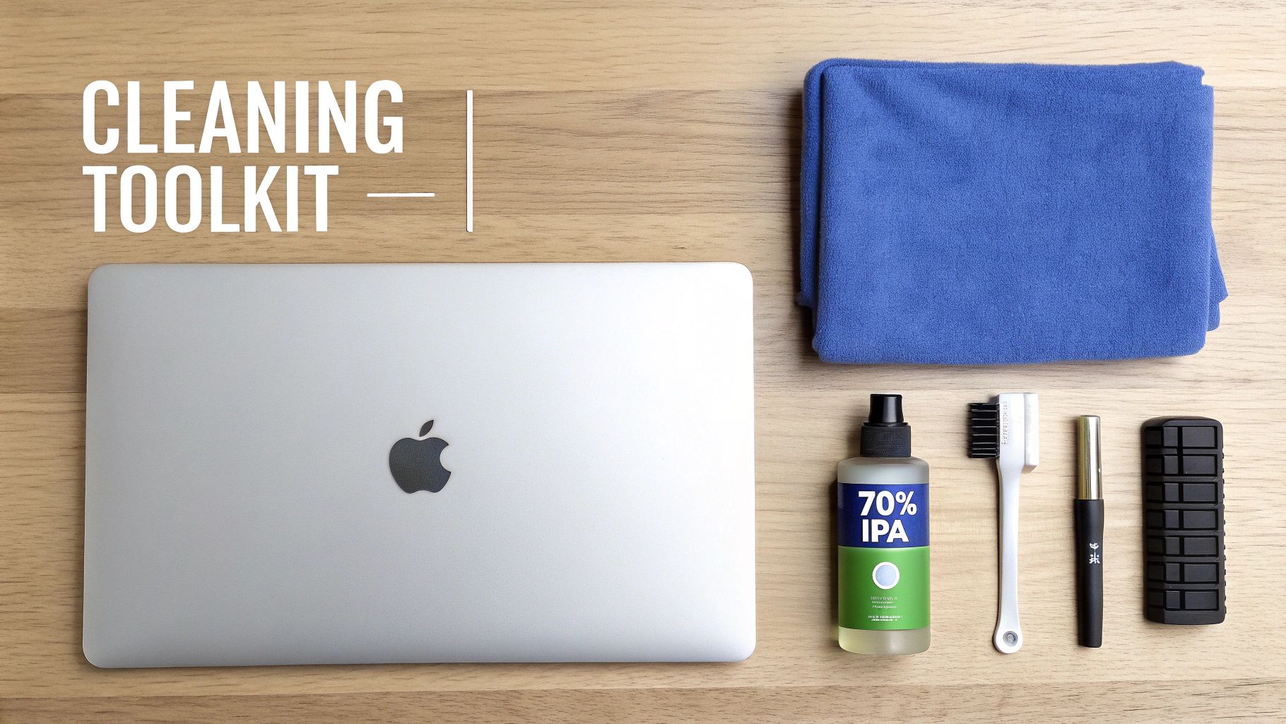 A flat lay of a MacBook cleaning toolkit showing a laptop, brush, IPA spray, cloth, and other tools on a wooden table.