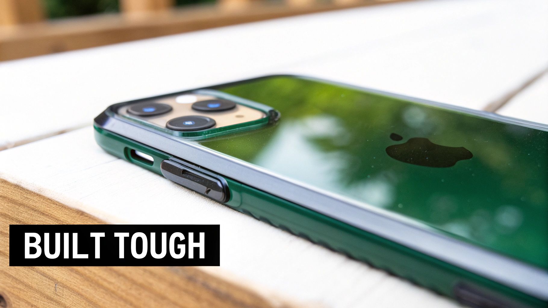 Close-up of a green iPhone in a protective case on a wooden surface, showing the Apple logo and cameras, with "BUILT TOUGH" text.