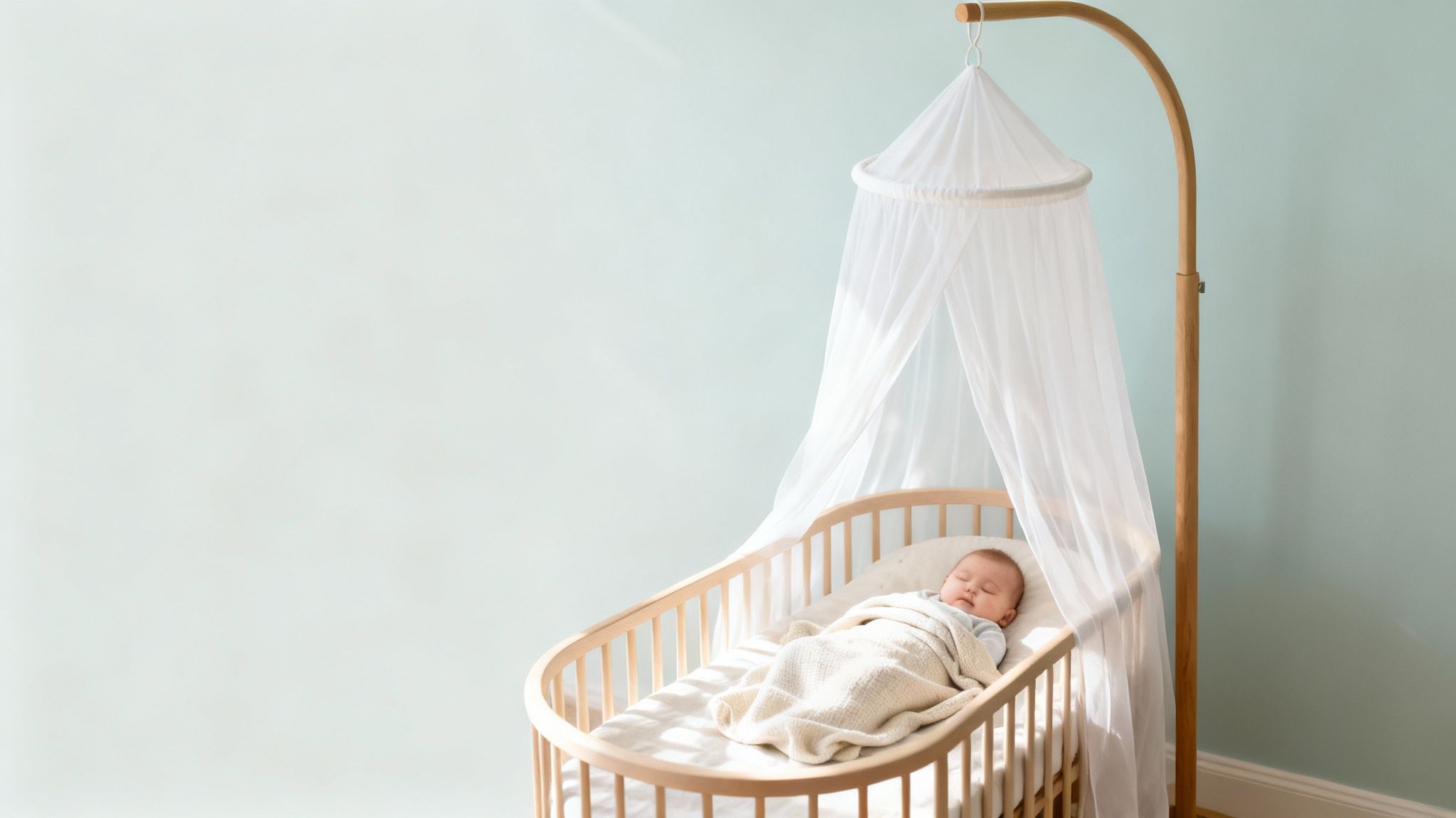 Slapende baby in houten wieg met witte klamboe en standaard voor een lichtblauwe muur.