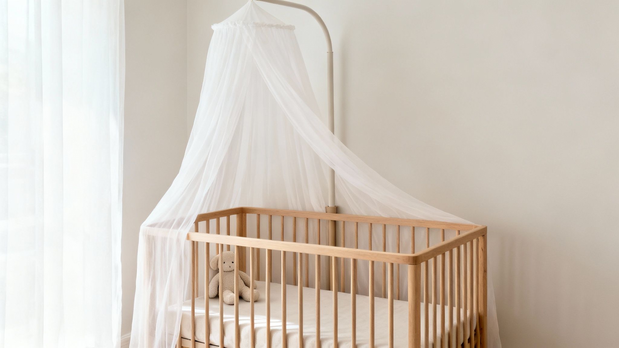Een minimalistische babykamer met een houten wiegje, een witte klamboe en een knuffel.