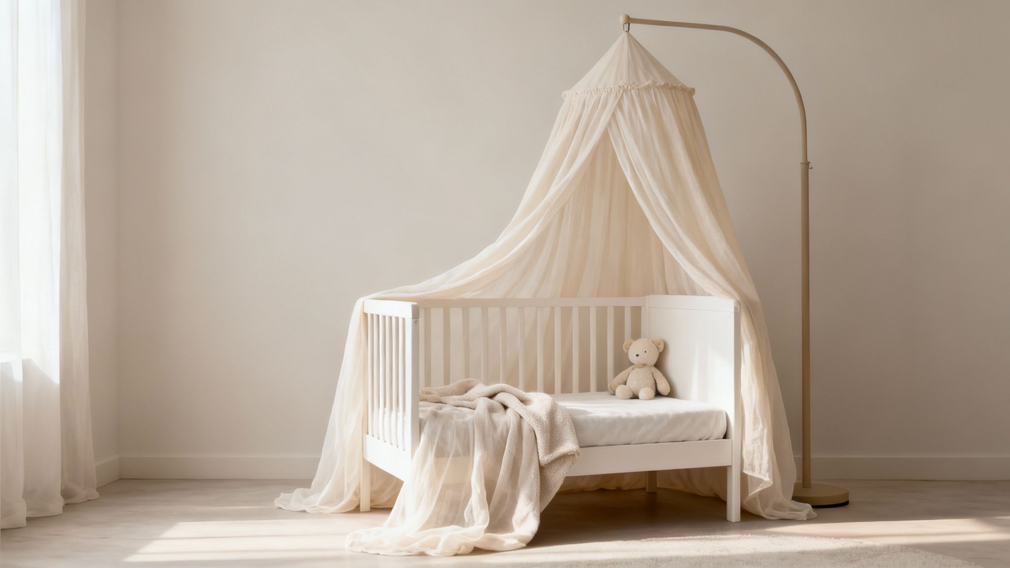 Witte babywieg met crèmekleurige klamboe op standaard en teddybeer in een lichte kinderkamer.