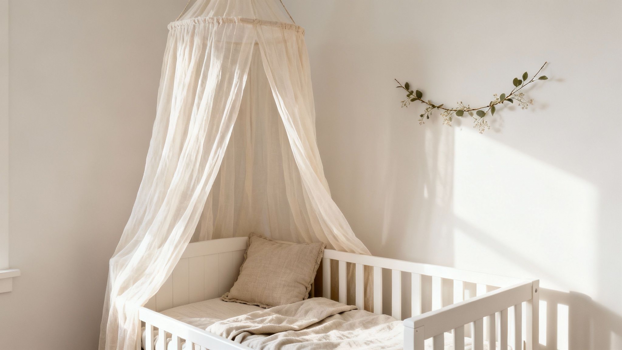 Witte babywieg met beige beddengoed en een lichte luifel in een zonnige babykamer.