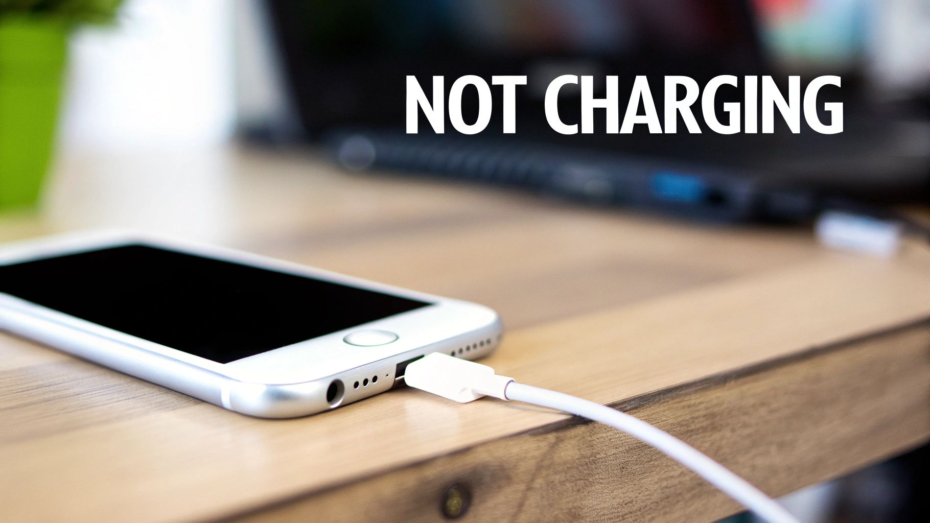 A silver iPhone connected to a white charger cable on a wooden desk, with text 'NOT CHARGING'.