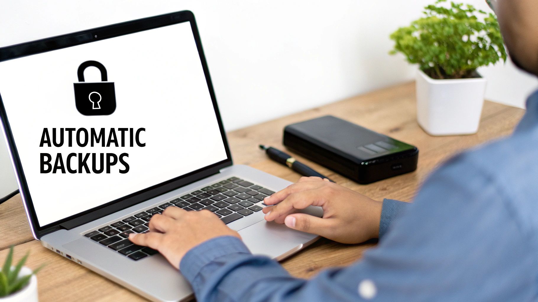 A person typing on a laptop with 'AUTOMATIC BACKUPS' displayed on the screen, next to an external hard drive.