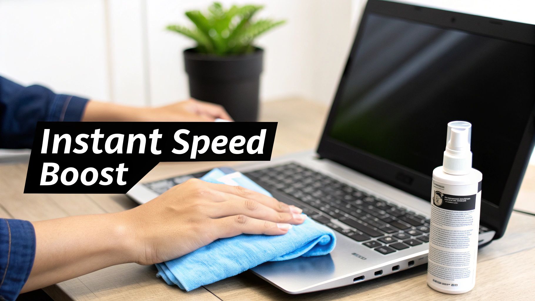 A person is cleaning a laptop with a blue microfiber cloth and cleaning spray on a wooden desk.