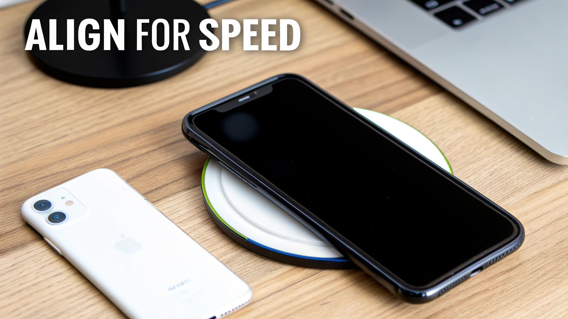 A black iPhone charges on a white wireless pad next to a white iPhone on a wooden desk.