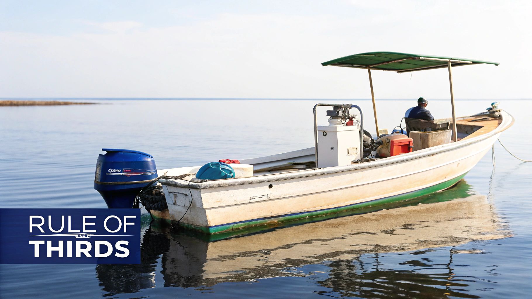 A small motorboat with a blue outboard engine and a person under a canopy floats on calm water.