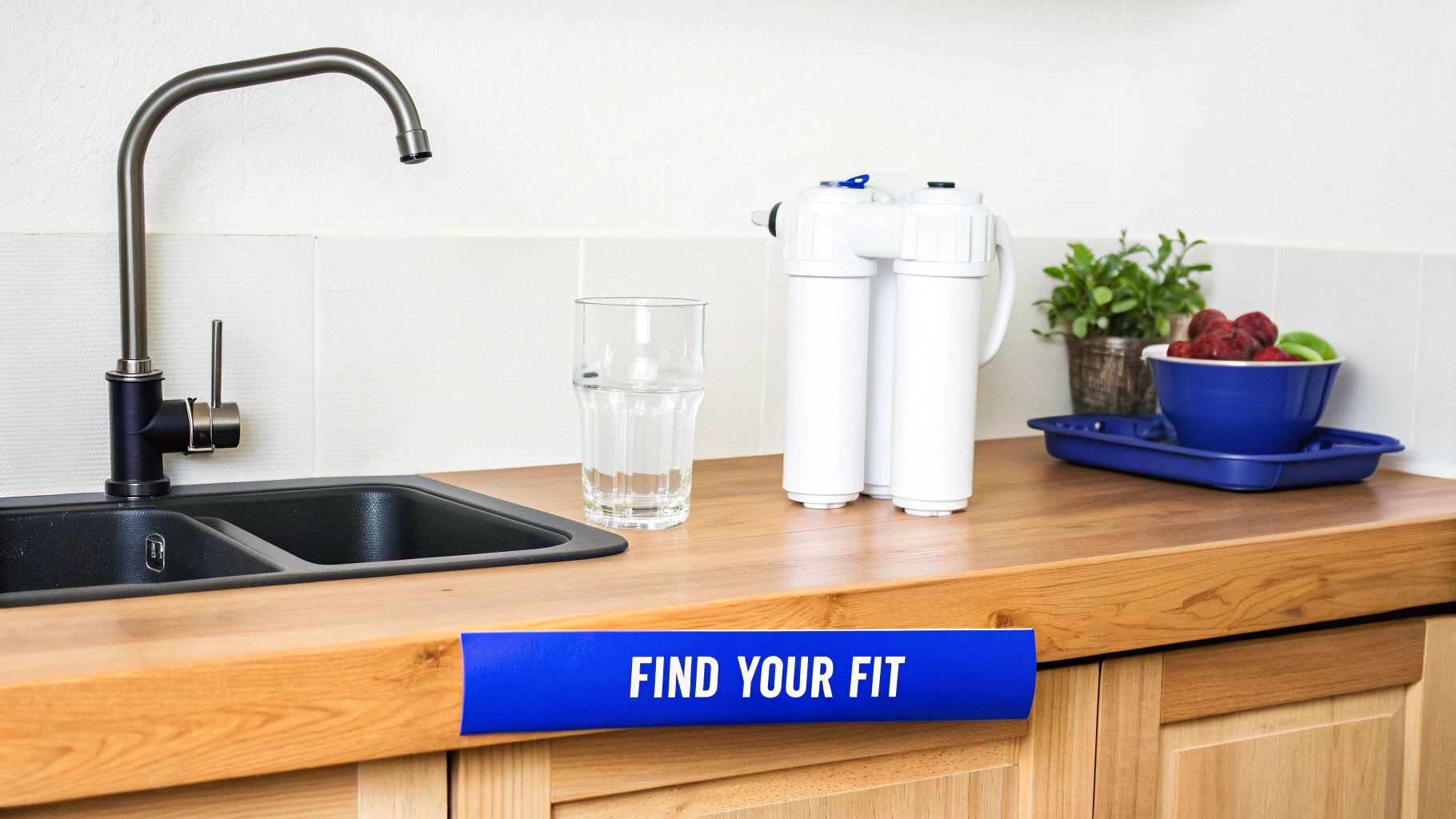 A clean kitchen counter with a sink, faucet, water filter, glass of water, and fruit.