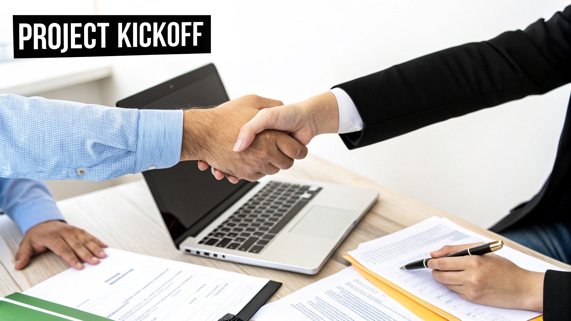 Two business professionals shake hands over a laptop and documents, signifying a project kickoff.