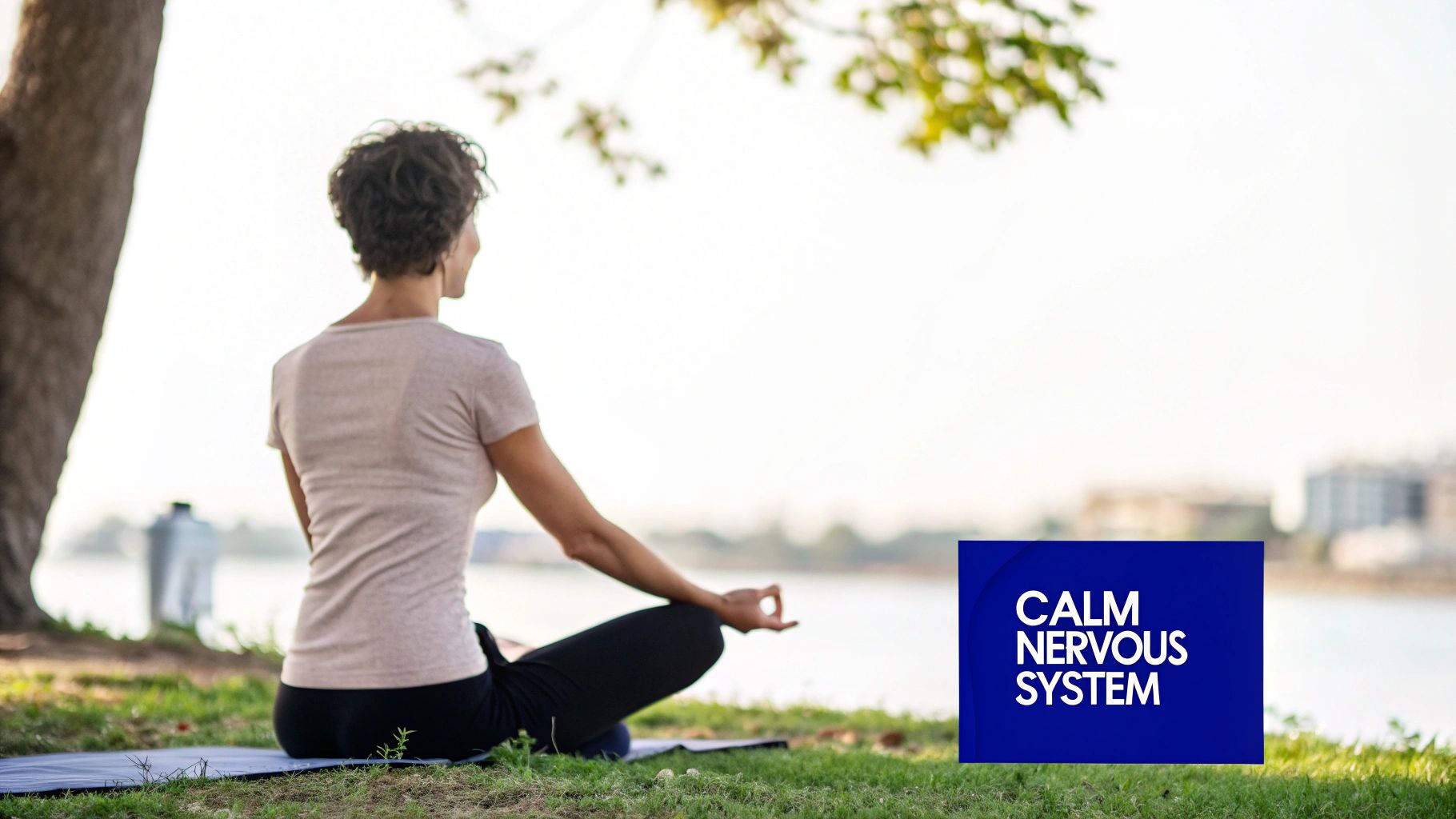 A woman meditates by a tranquil lake, practicing yoga outdoors on a mat, promoting a calm nervous system.