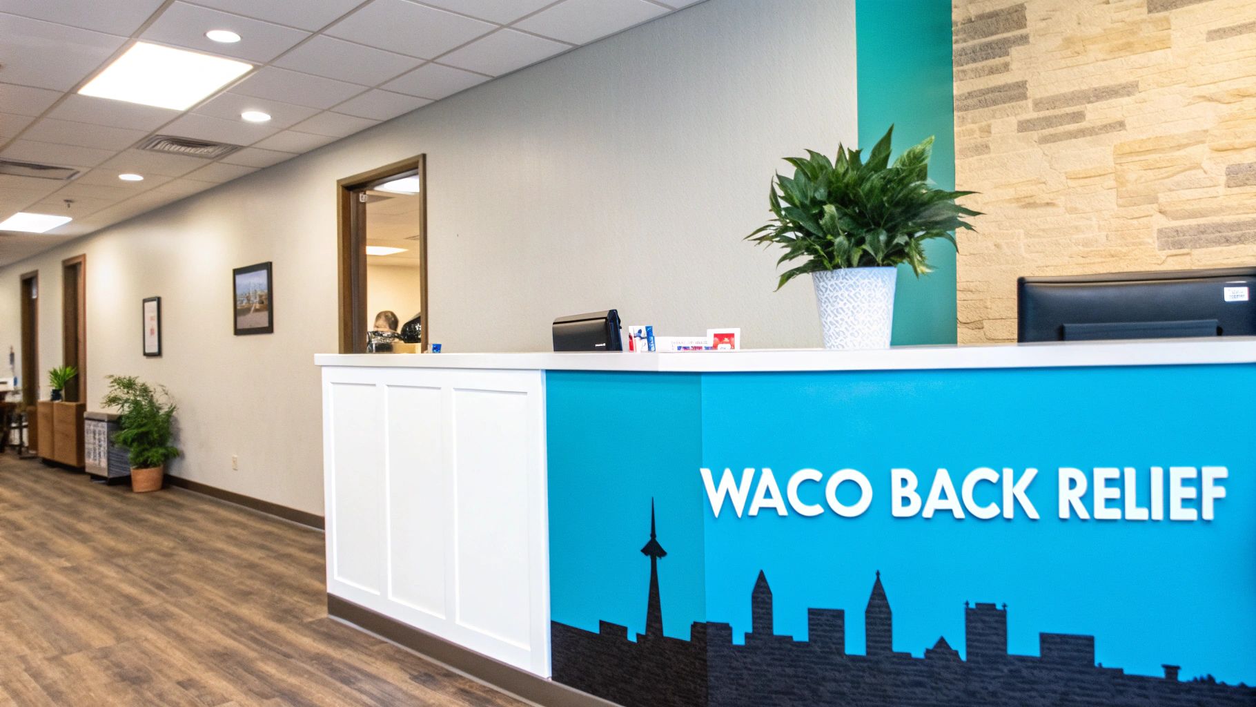 A bright and clean reception area with a blue desk featuring 'WACO BACK RELIEF' text and a plant.