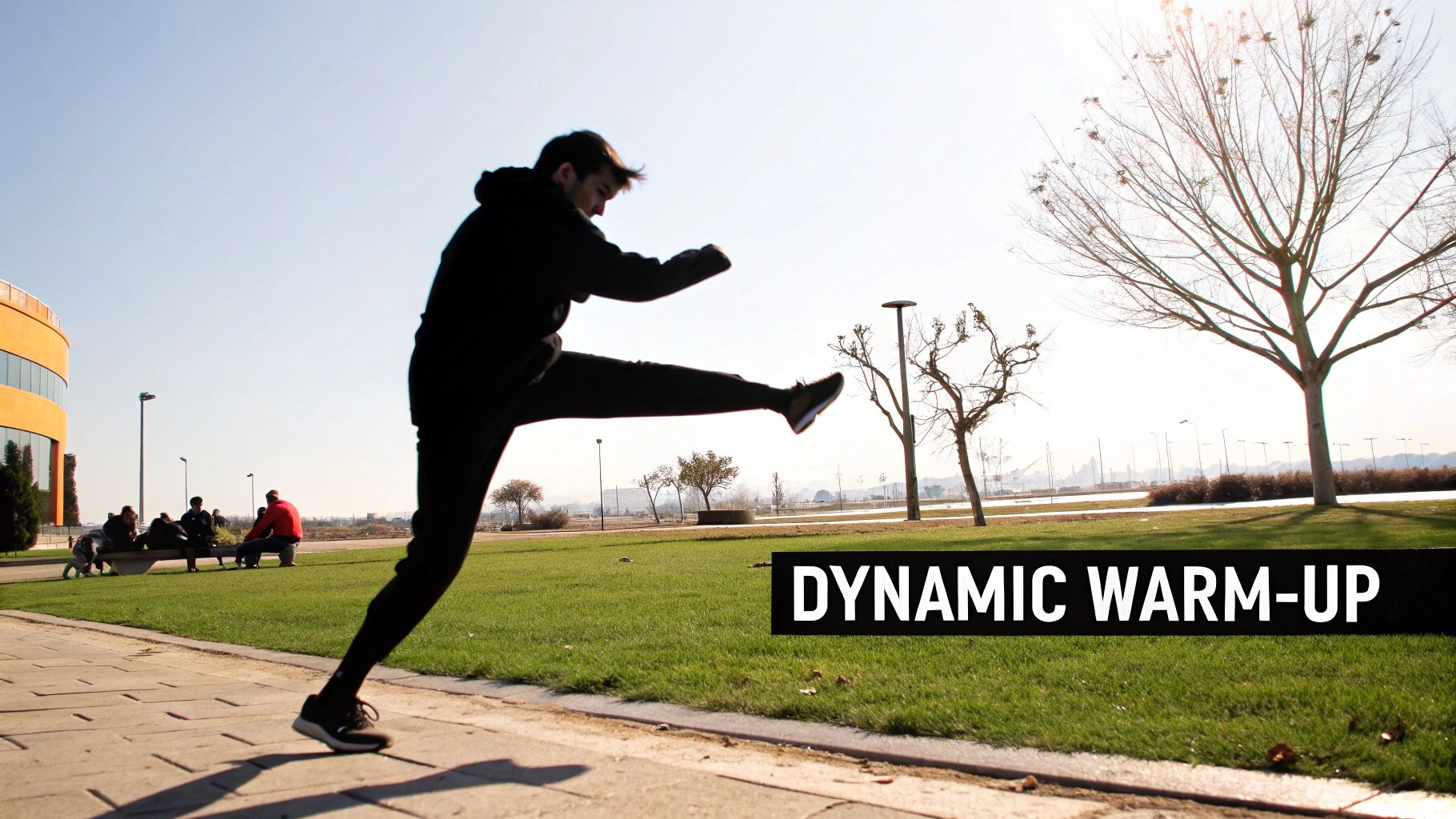 A person in black clothing performs a dynamic warm-up exercise with a high leg kick in a park on a sunny day.