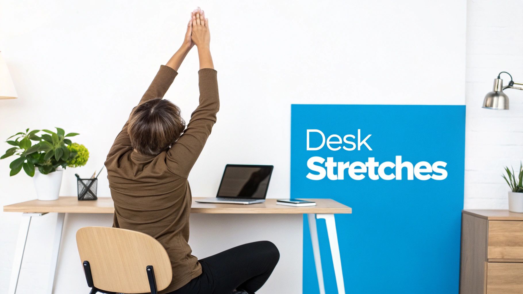 A person sitting at a desk, stretching their arms upwards, with a laptop and plants.
