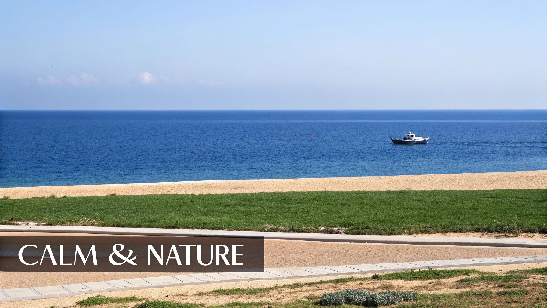 A serene coastal landscape with a sandy beach, green grass, a calm blue sea, and a white boat moving.