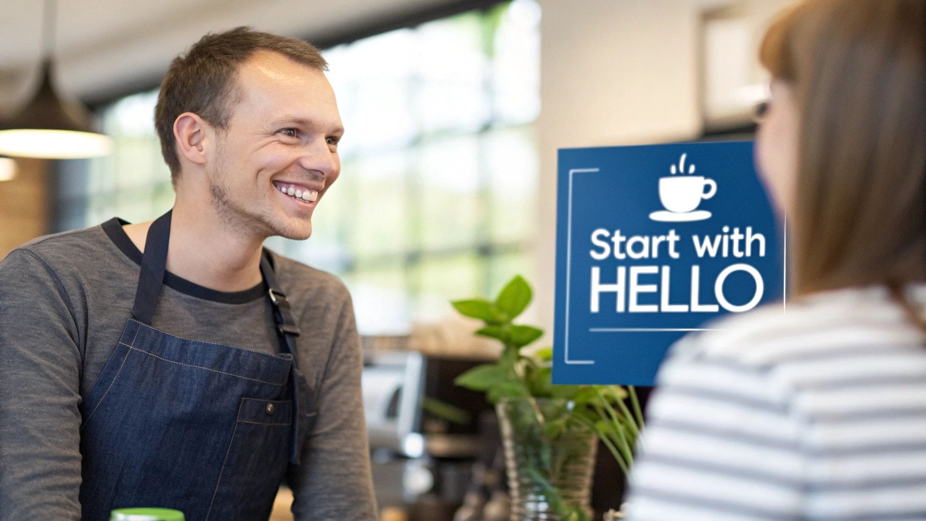 A smiling male barista in an apron greets a female customer at a coffee shop, with a 'Start with HELLO' sign.