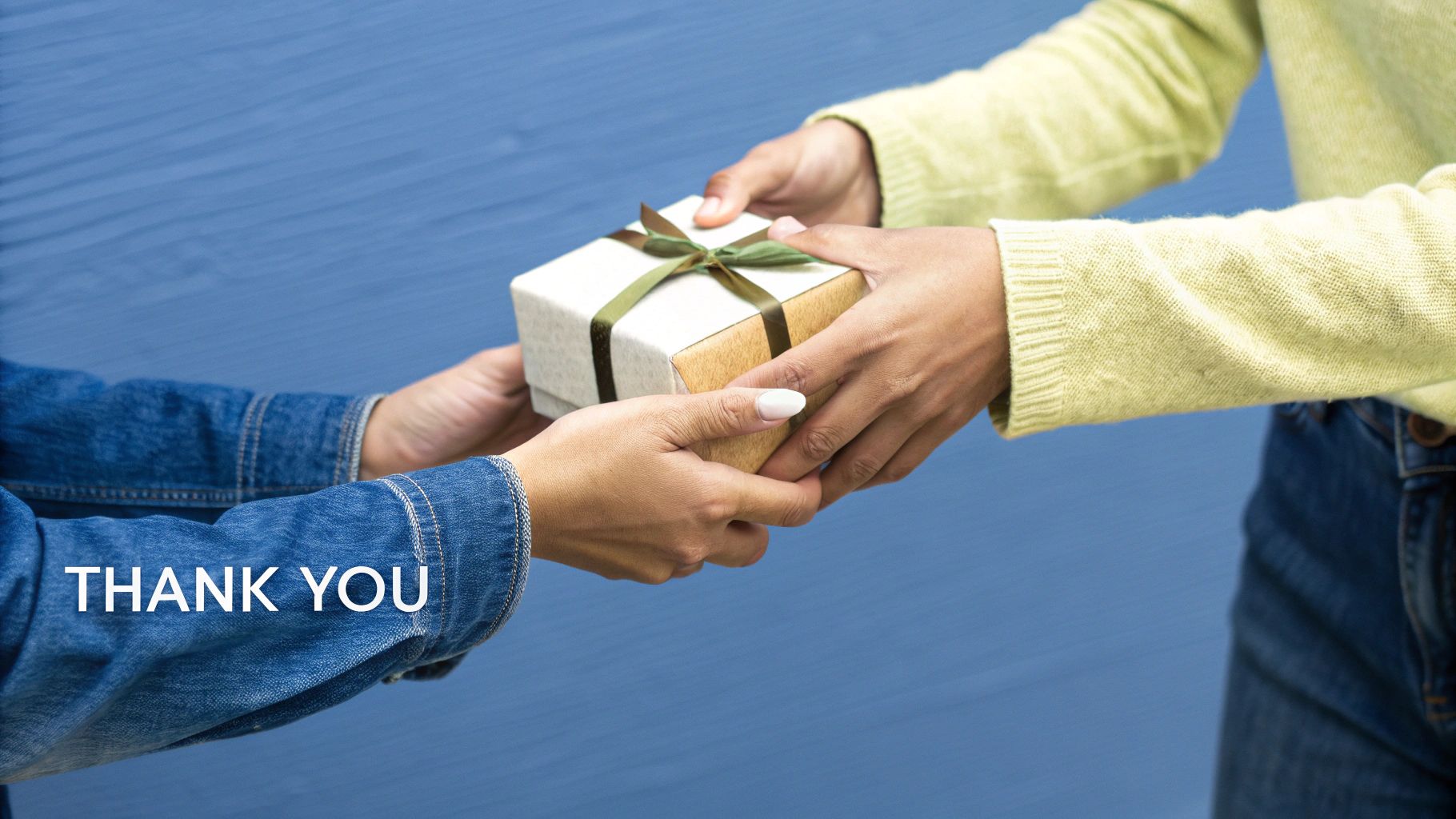 Close-up of two people's hands exchanging a small gift box with a green ribbon.