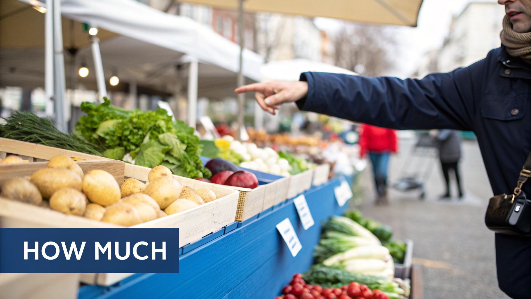 A person points at fresh potatoes and leafy green vegetables displayed at an outdoor market stall.