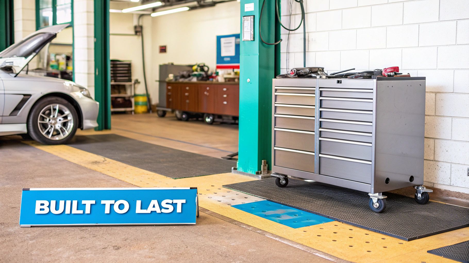 A spacious automotive workshop with a car, large gray tool cabinet, and 'BUILT TO LAST' sign.