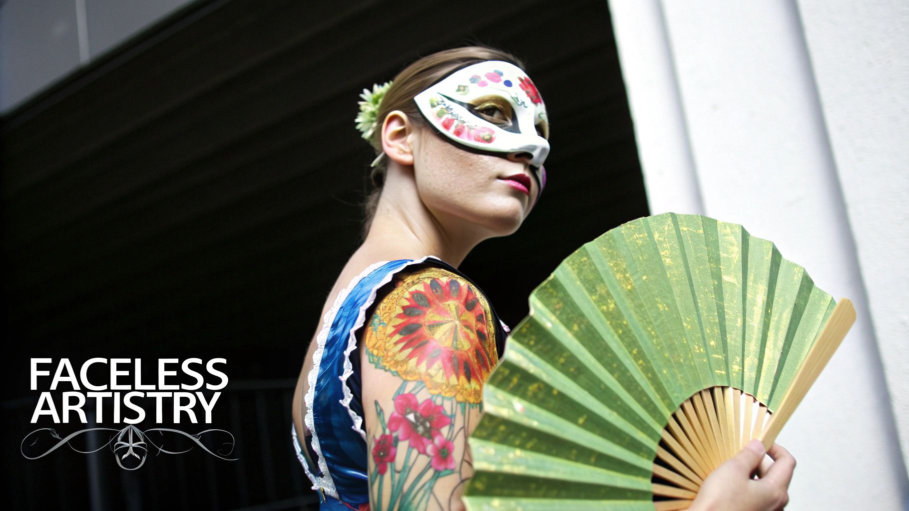 A woman with a decorative mask, vibrant arm tattoo, and a green fan, embodying artistry.