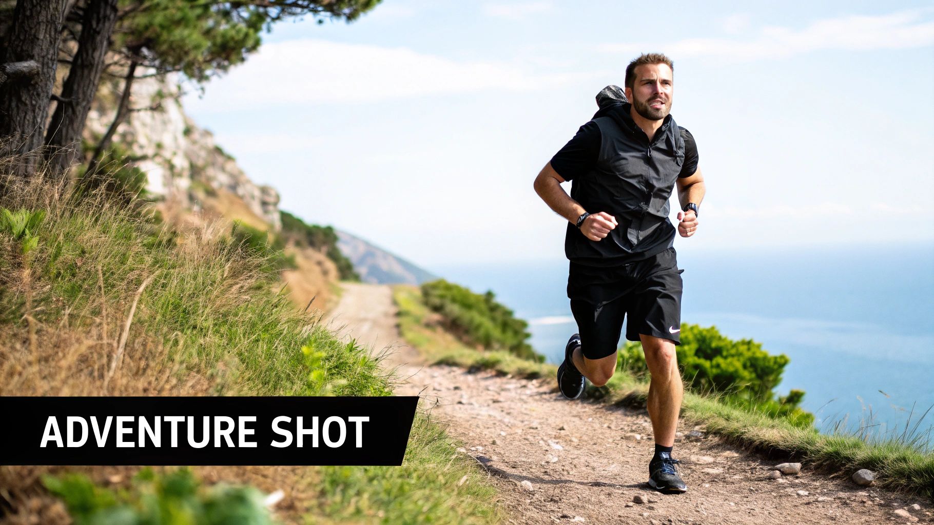 A man runs on a scenic mountain trail overlooking the ocean, enjoying an outdoor adventure.