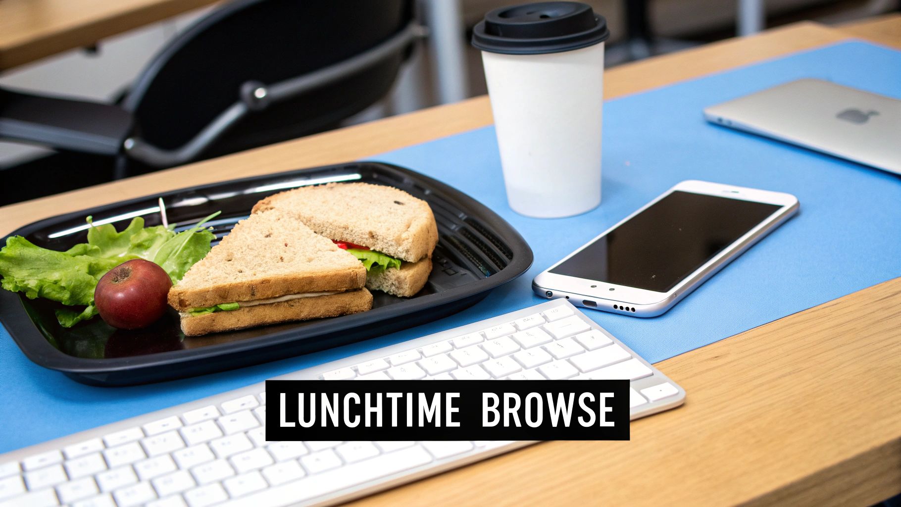 A lunch break scene with a sandwich, coffee, smartphone, and keyboard on a desk.