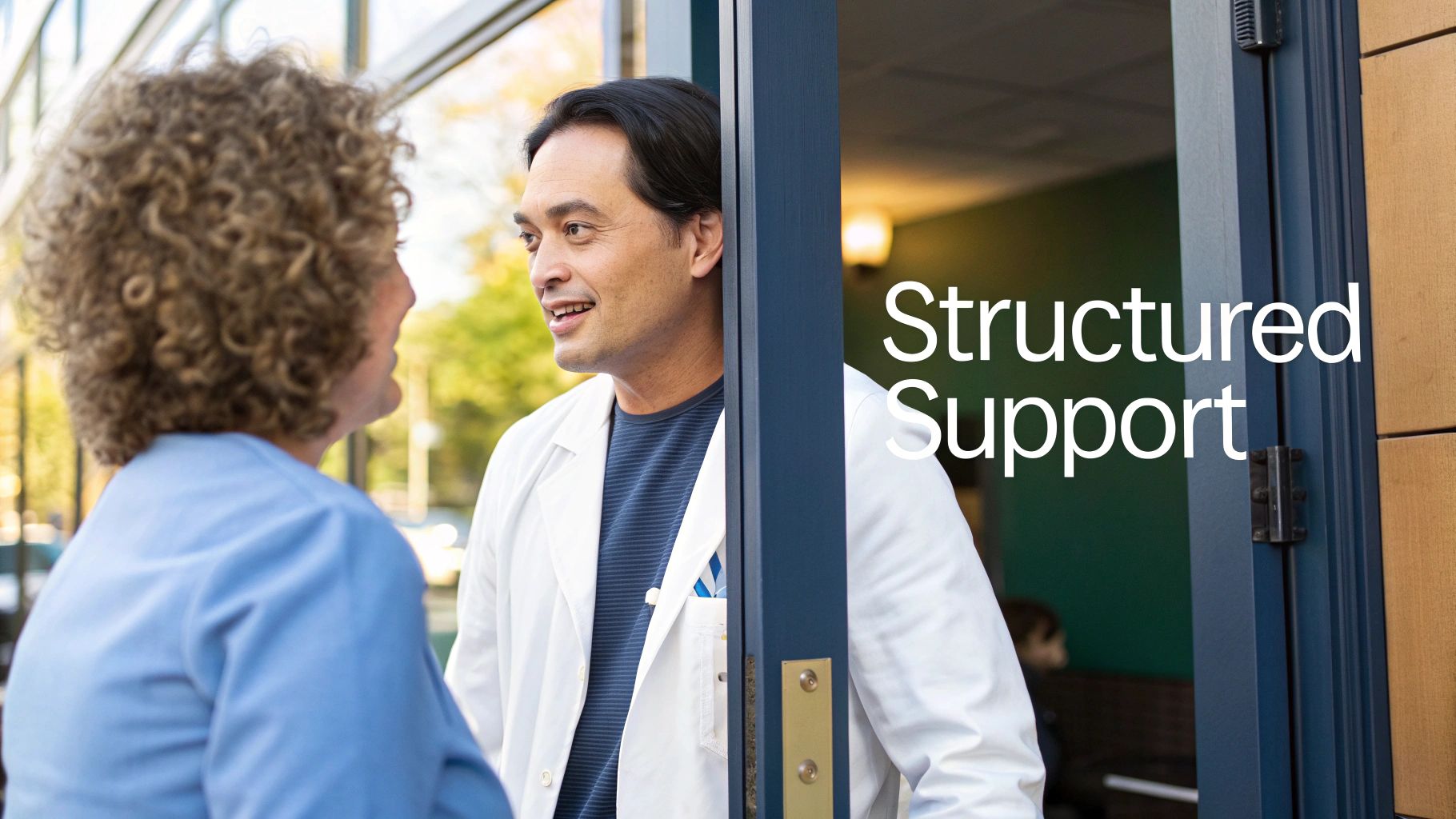 Two healthcare professionals, a man in a lab coat and a woman, smiling and talking in a doorway.