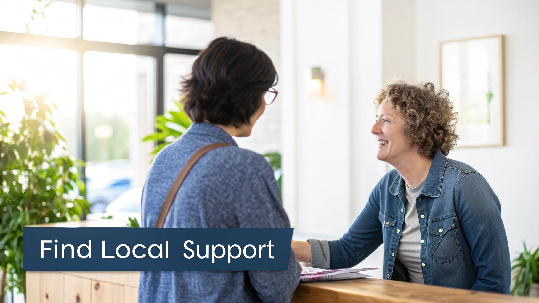 A smiling woman with curly hair helps another client at a counter, reflecting local support services.