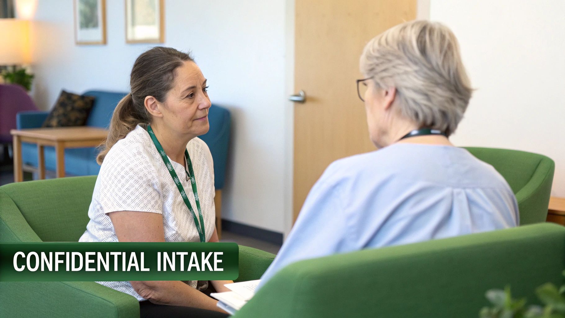 Two women engage in a confidential intake session in a comfortable lounge setting.