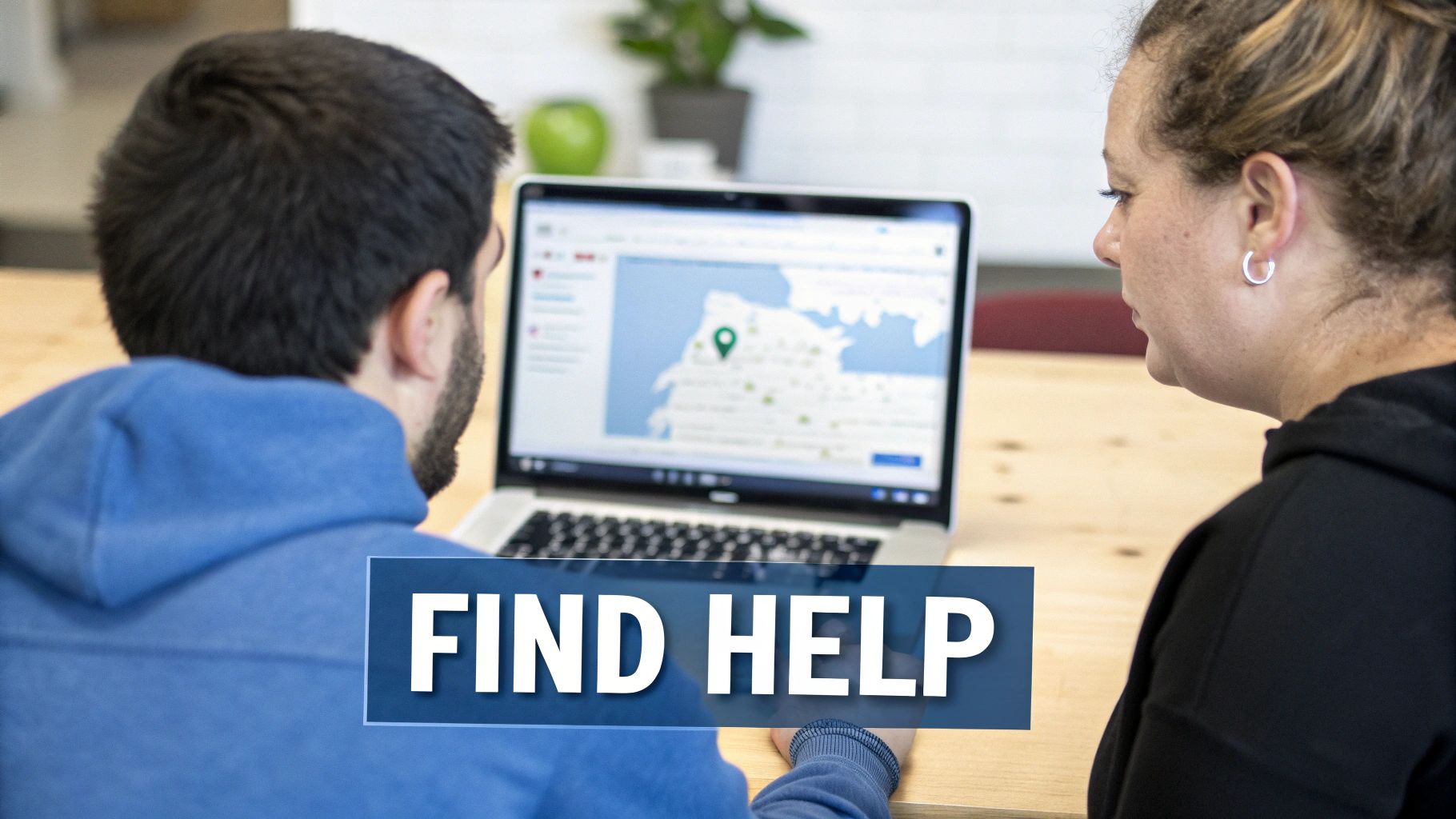 A person researching on a laptop with a supportive friend nearby