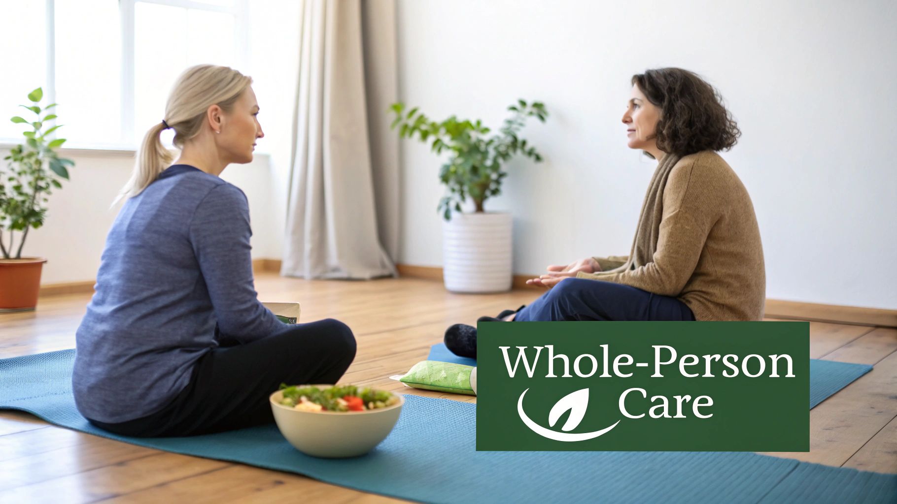 Two women sit on yoga mats, facing each other, with a salad, representing whole-person care.