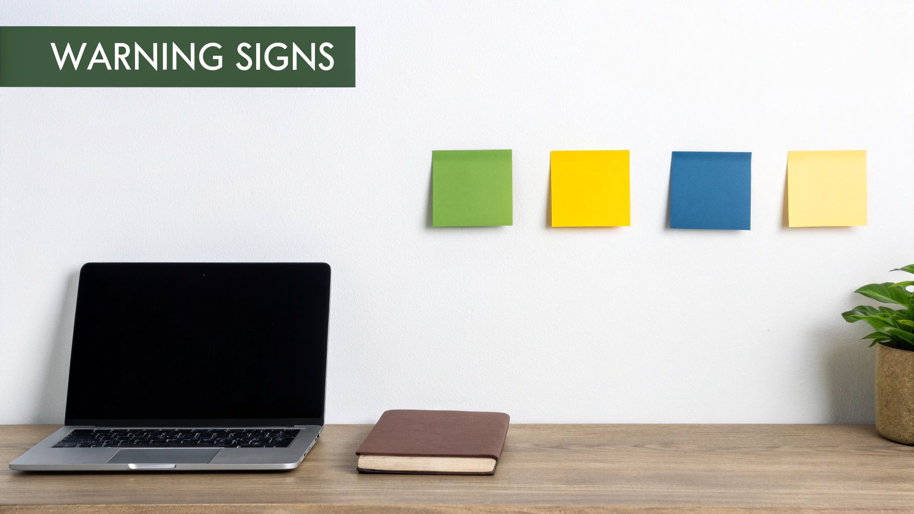Office workspace with laptop, notebooks, colorful sticky notes on white wall labeled warning signs