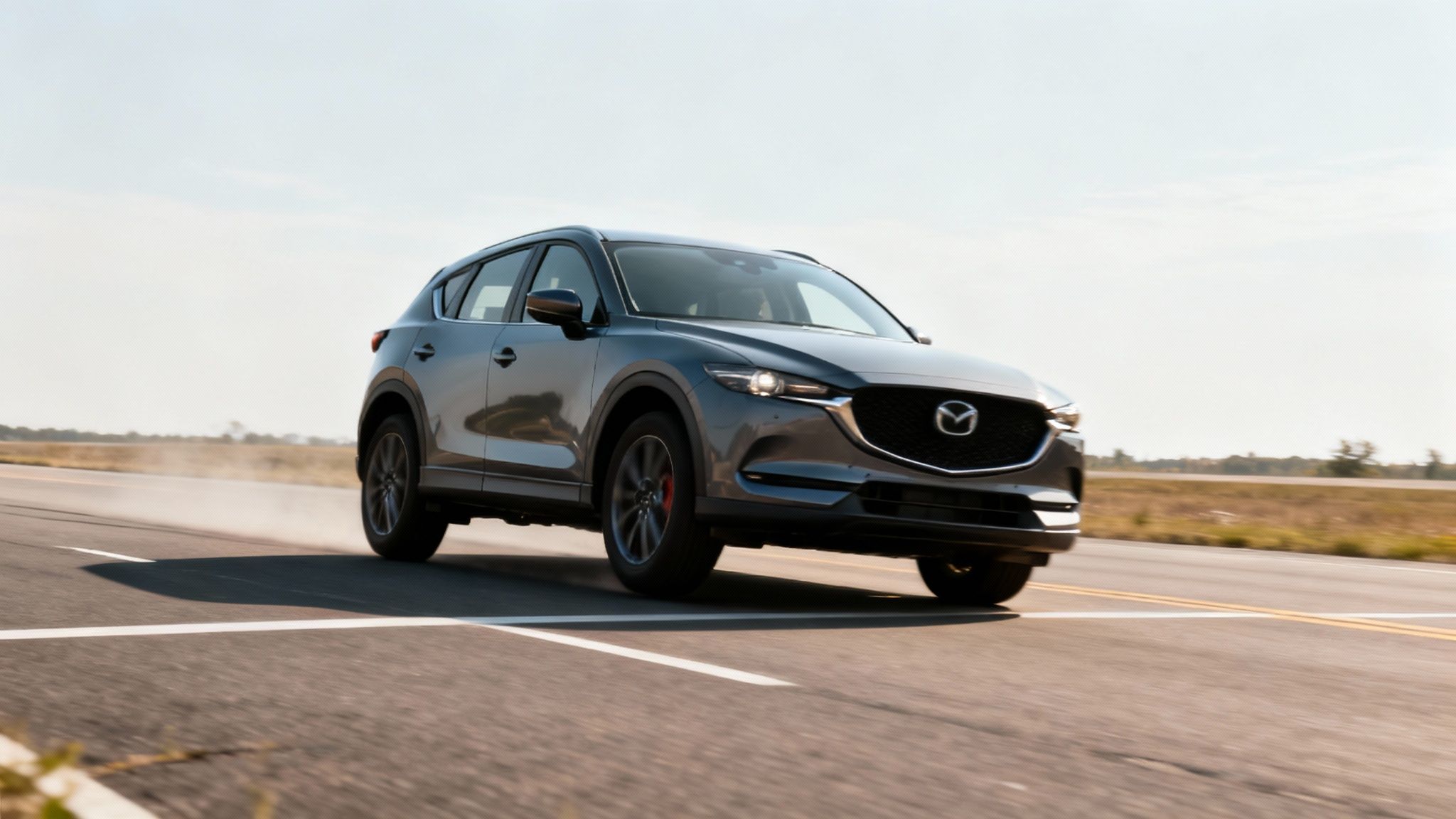 A dark grey Mazda CX-5 SUV speeds down a road, with motion blur and dust.