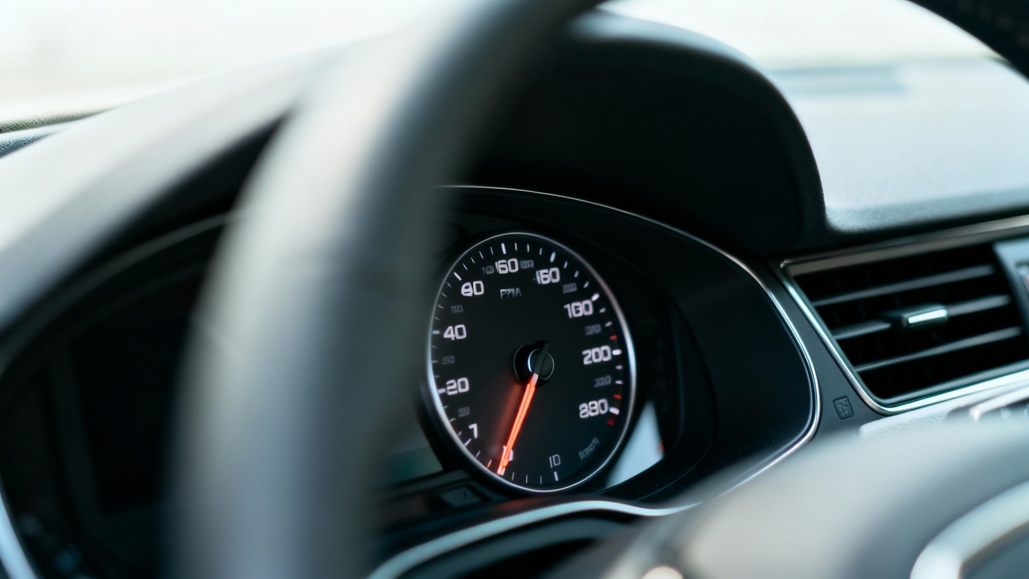Close-up view of a car's dashboard with speedometer and tachometer, seen through the steering wheel.