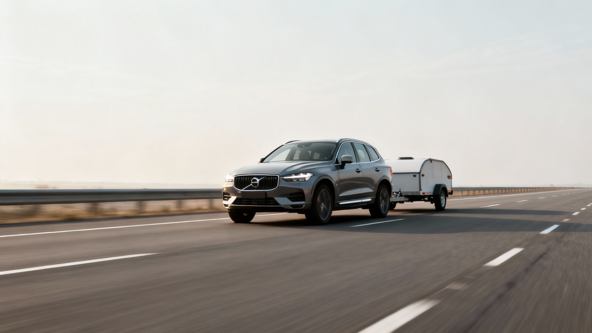 Modern grey SUV towing a small white camper on a multi-lane highway.