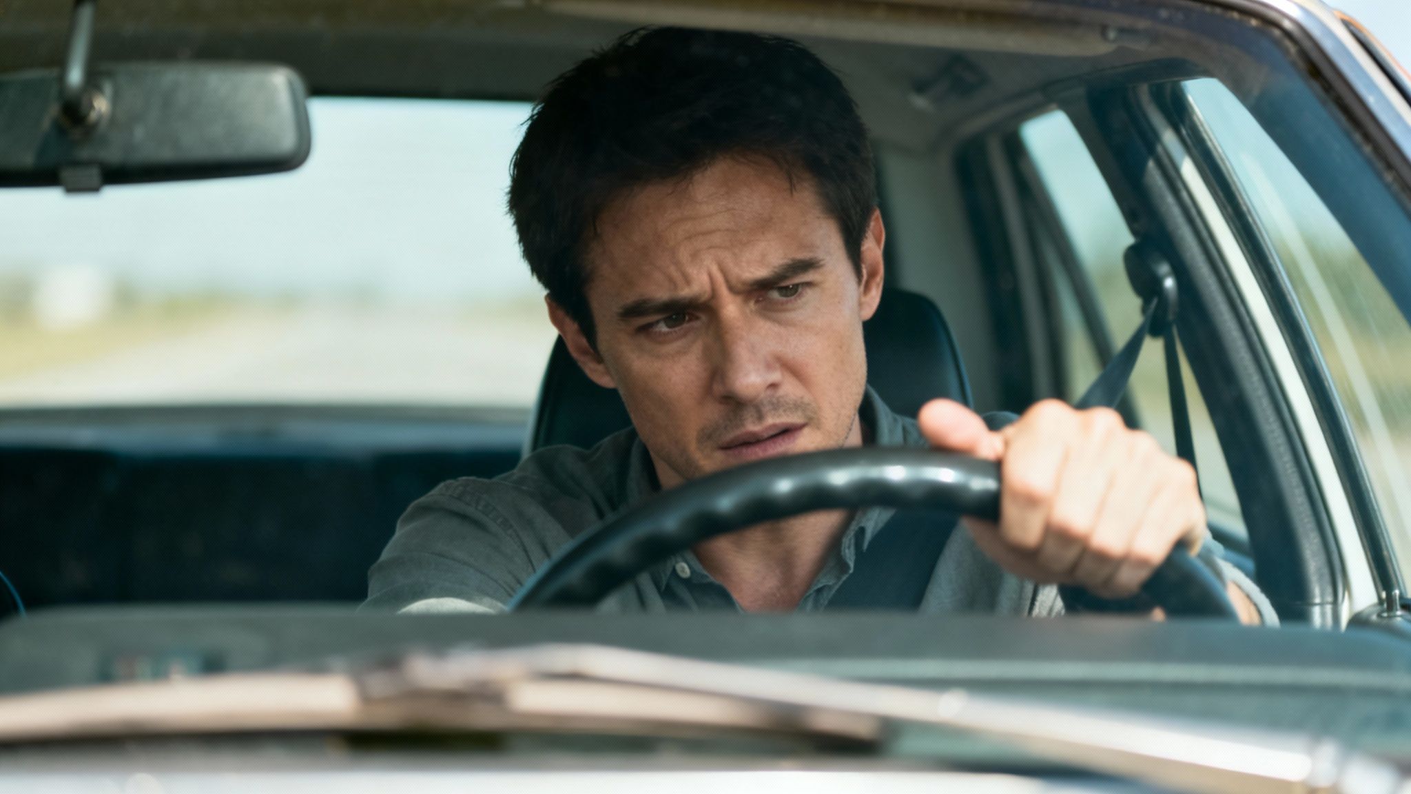A concerned man behind the wheel of a car, hands on the steering wheel, driving.