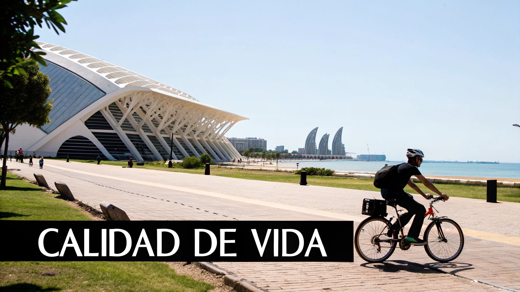 Ciclista en un paseo marítimo con arquitectura moderna y el mar azul bajo un cielo despejado.