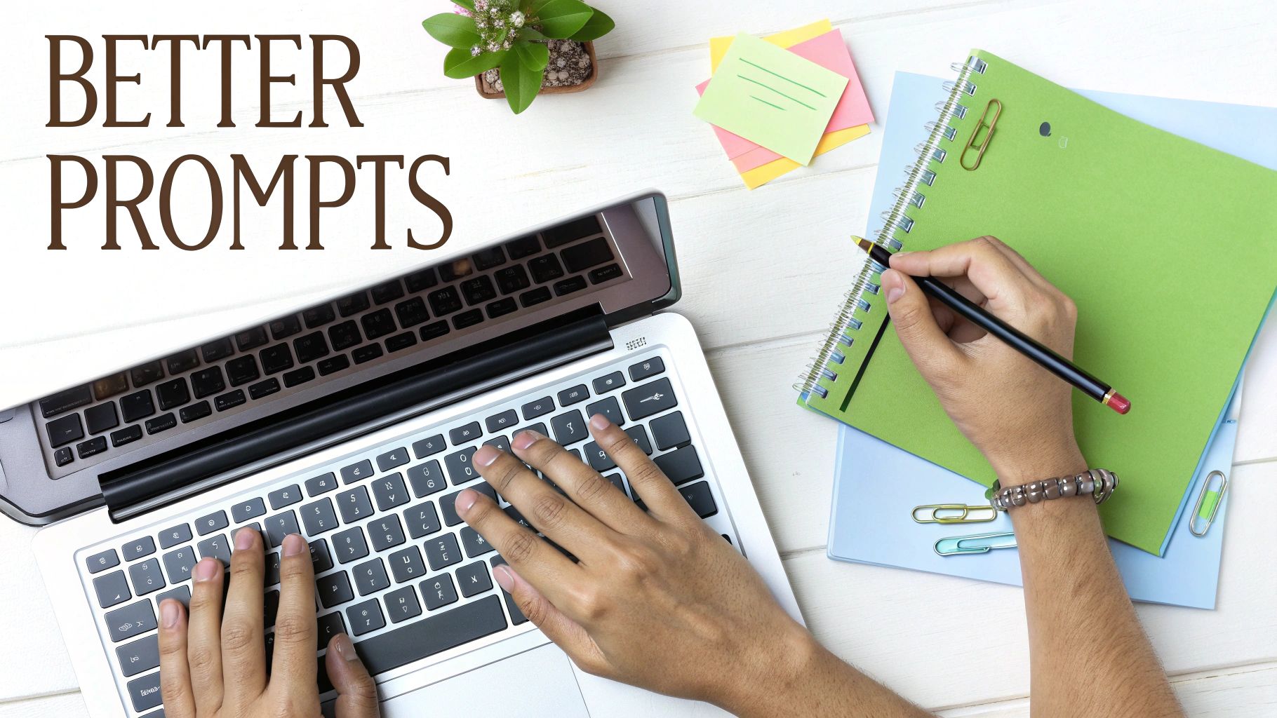 Overhead view of hands typing on a laptop and writing in a notebook, with 'BETTER PROMPTS' text.