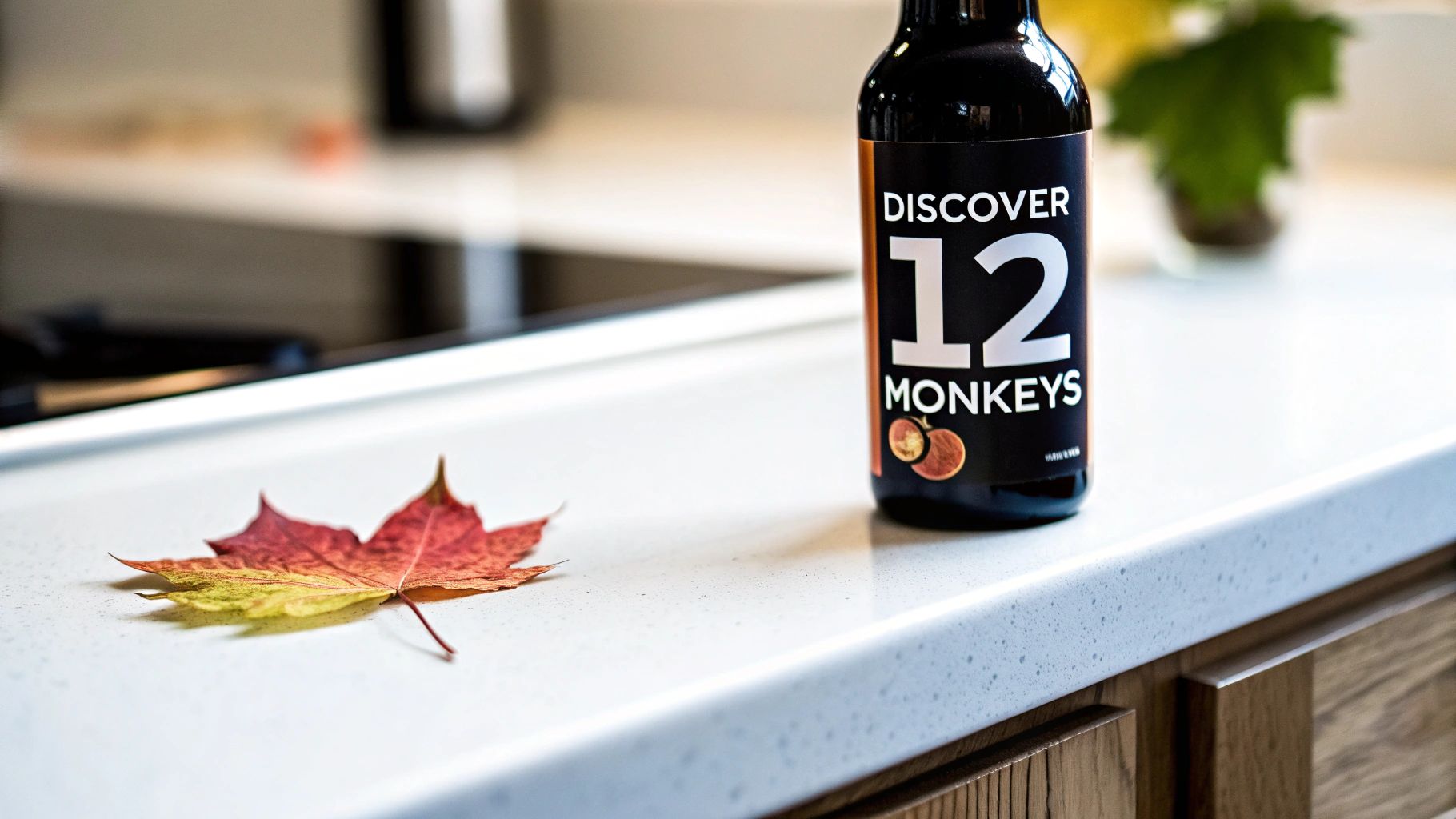 A black bottle of 'Discover 12 Monkeys' juice stands on a white countertop next to a vibrant autumn leaf.