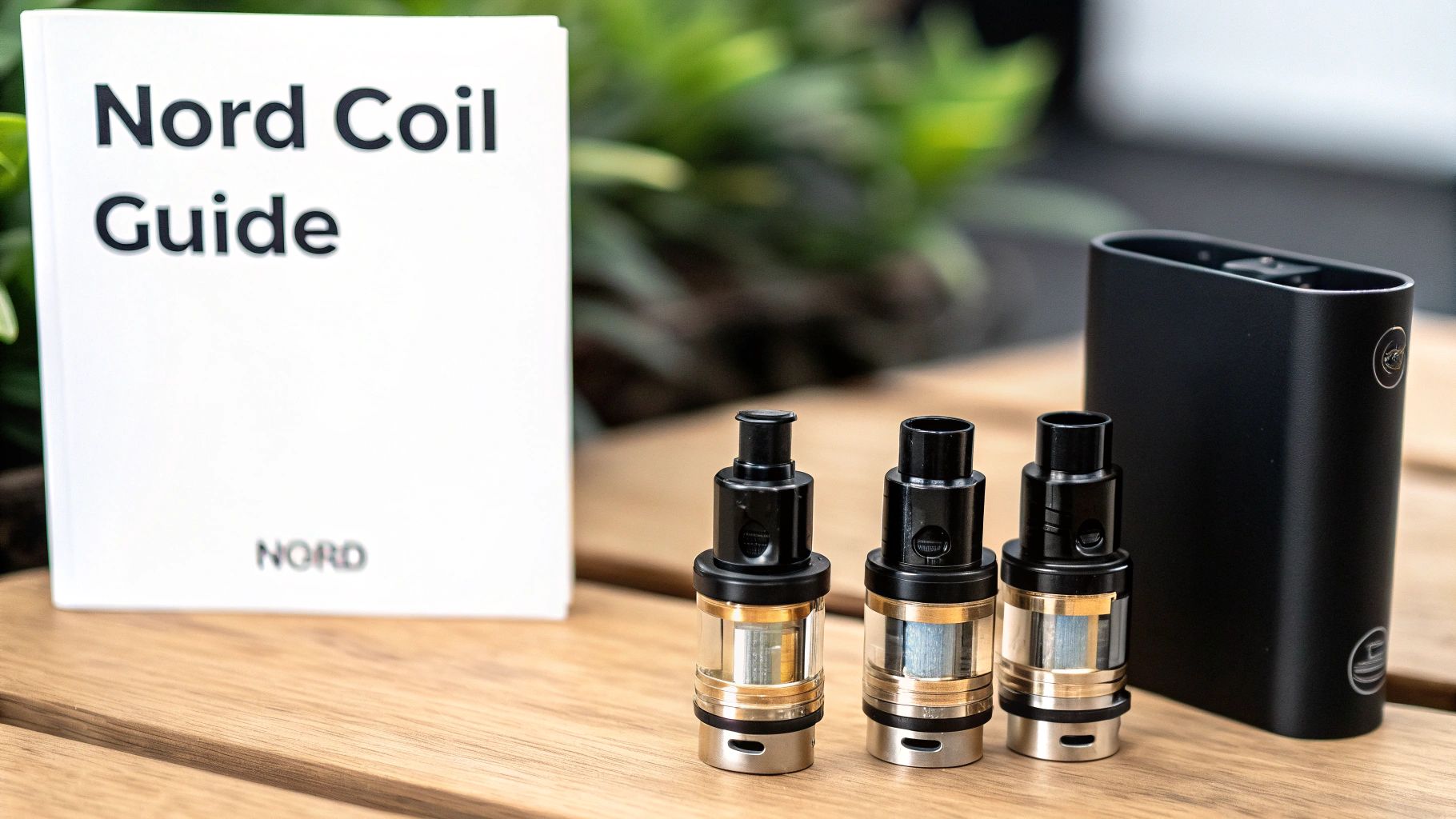 A Nord Coil Guide booklet, three vape tanks, and a black vape mod on a wooden surface.