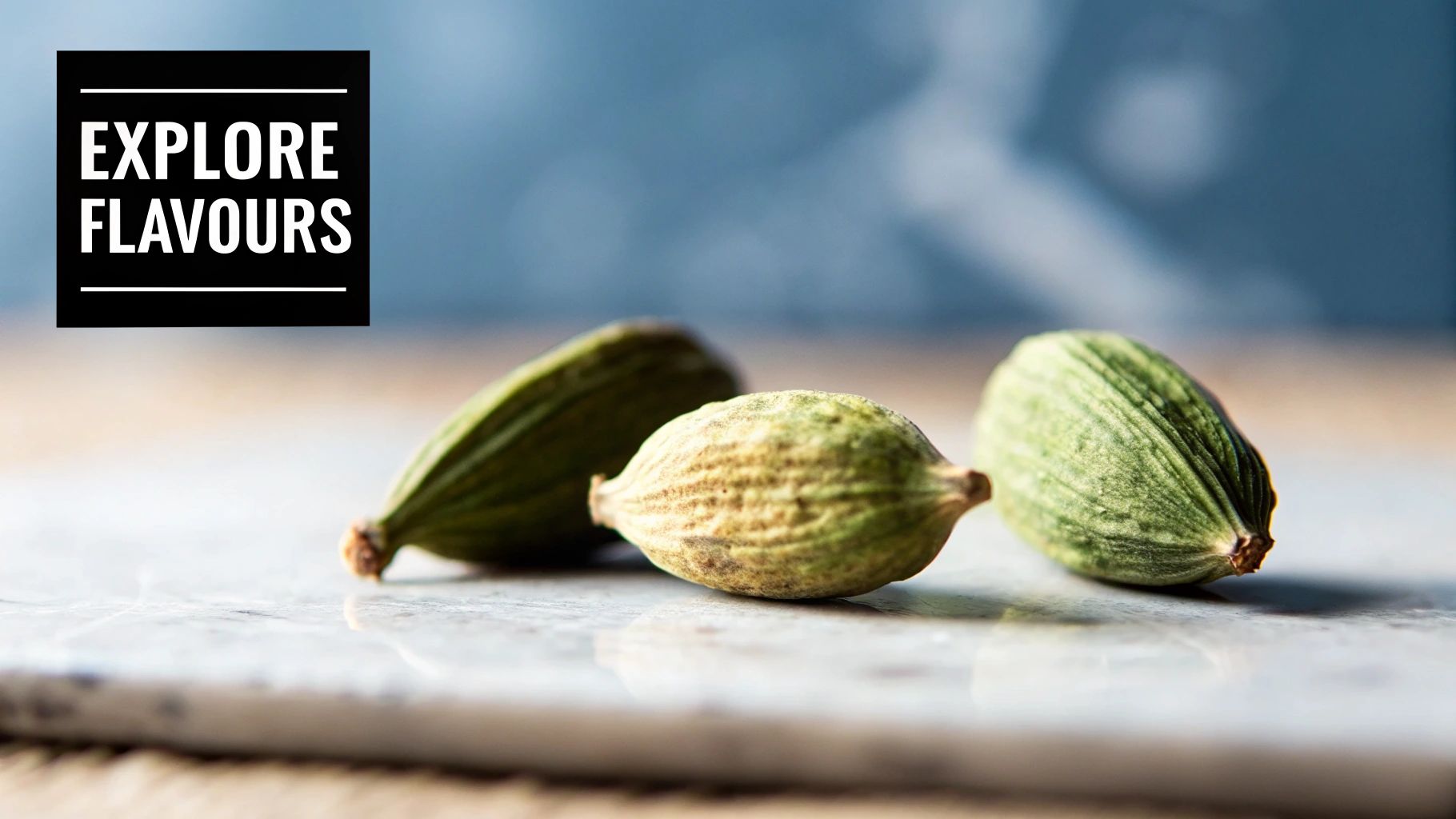 Close-up of three vibrant green cardamom pods on a light marble surface with a blurred background.