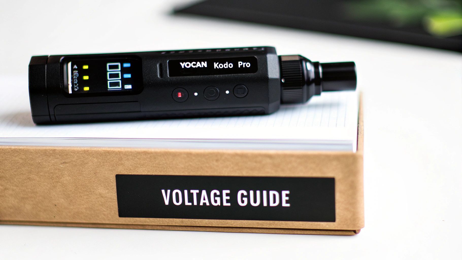 A black YOCAN Kodo Pro vape device with a digital display, resting on a notebook above a 'VOLTAGE GUIDE' box.