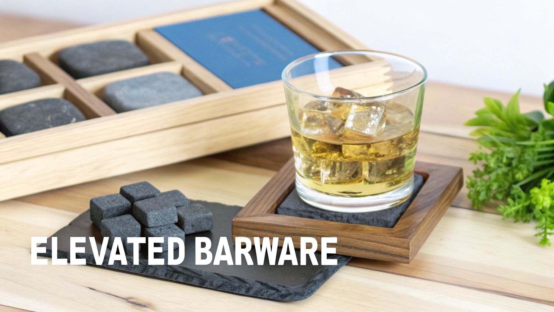 A whiskey glass with ice on a coaster, whiskey stones, and a wooden barware set on a table.