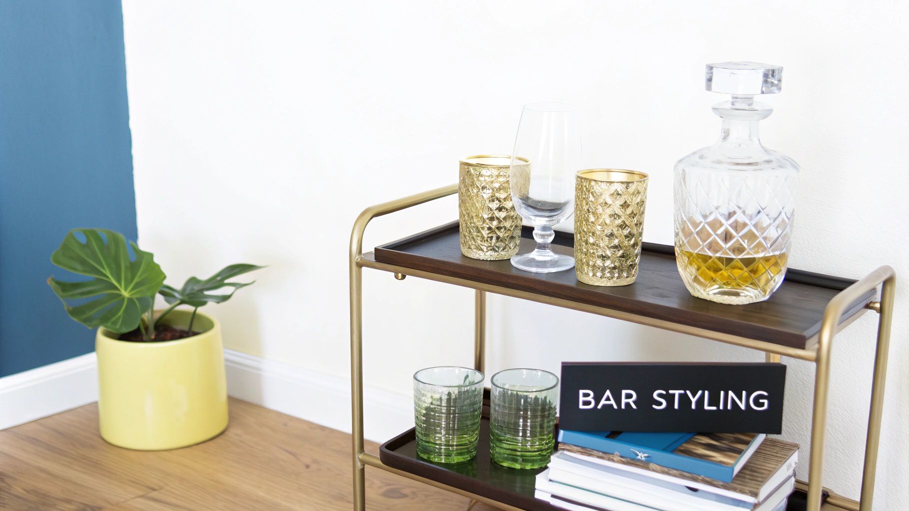 A stylish bar cart featuring gold and green glasses, a decanter of whiskey, and a "BAR STYLING" sign.