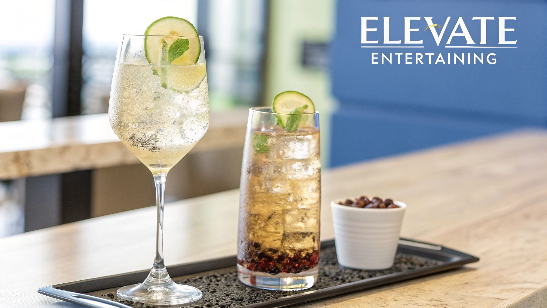 Elegant stemmed glass and a highball cocktail with garnishes and a snack on a serving tray.